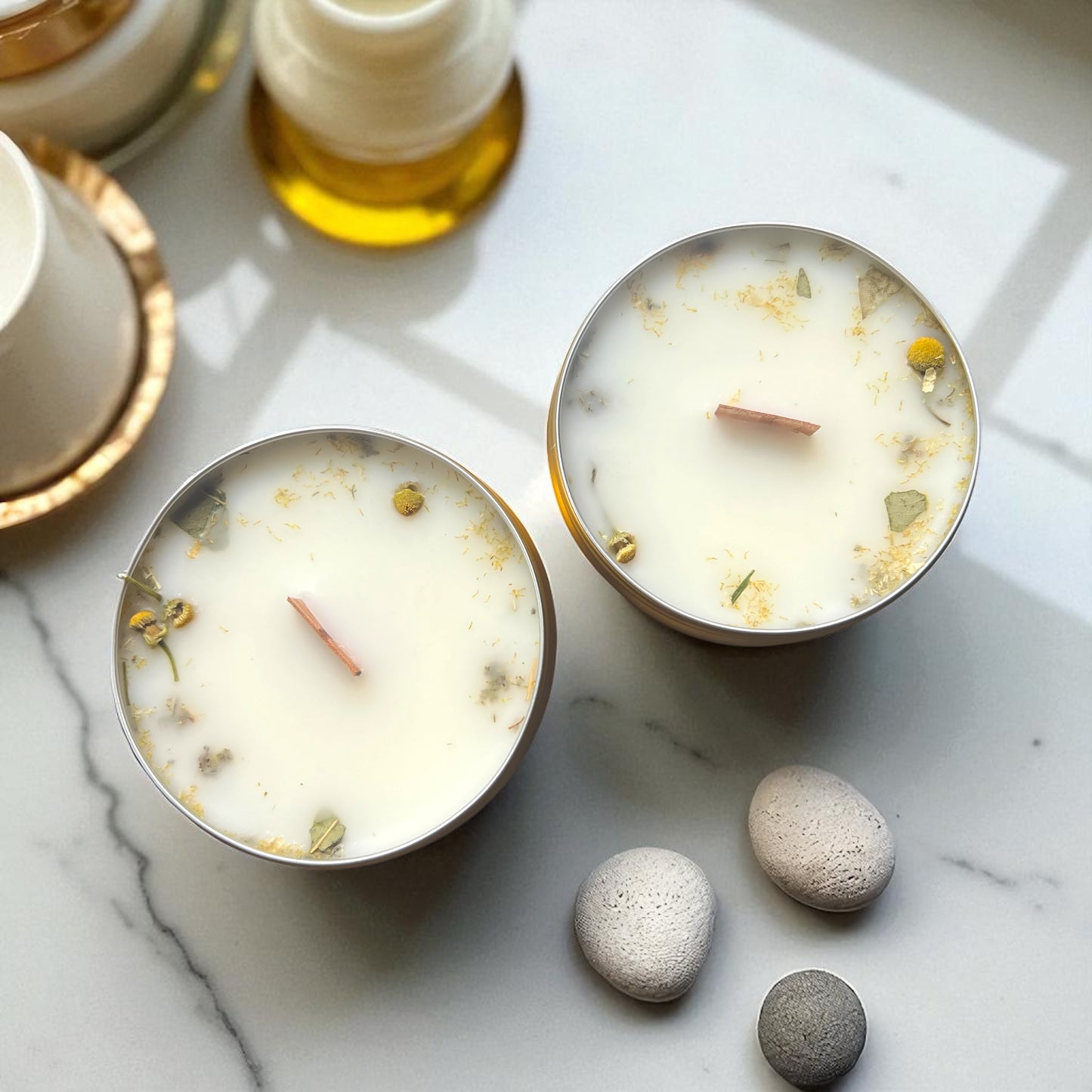 Two small candles with decorative elements on a marble surface with stones.