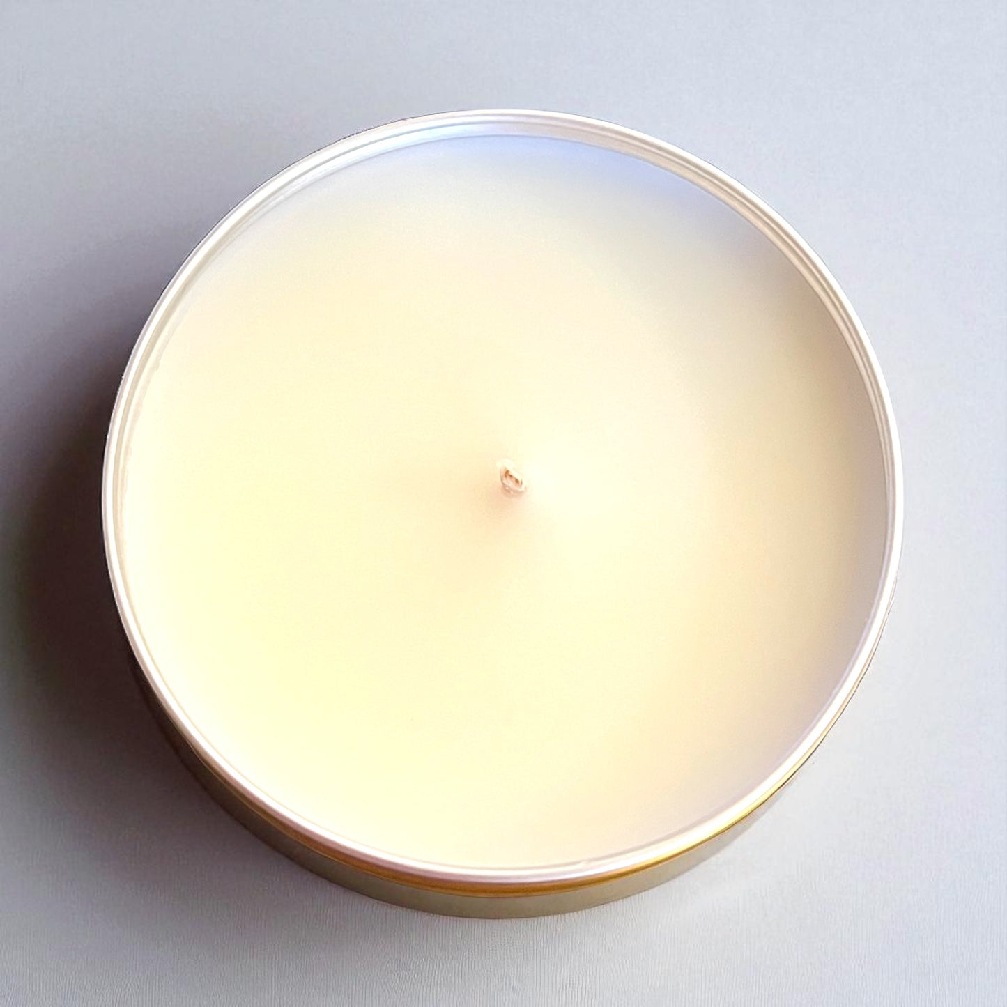 Round candle in a tin container on a light gray background