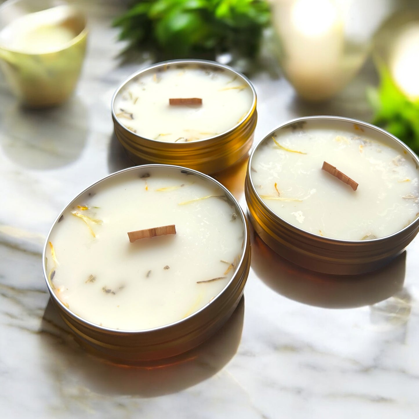 Three small candles in metal tins on a marble surface with greenery in the background.