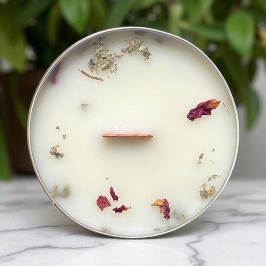 Candle in a metal container with dried flowers on a marble surface