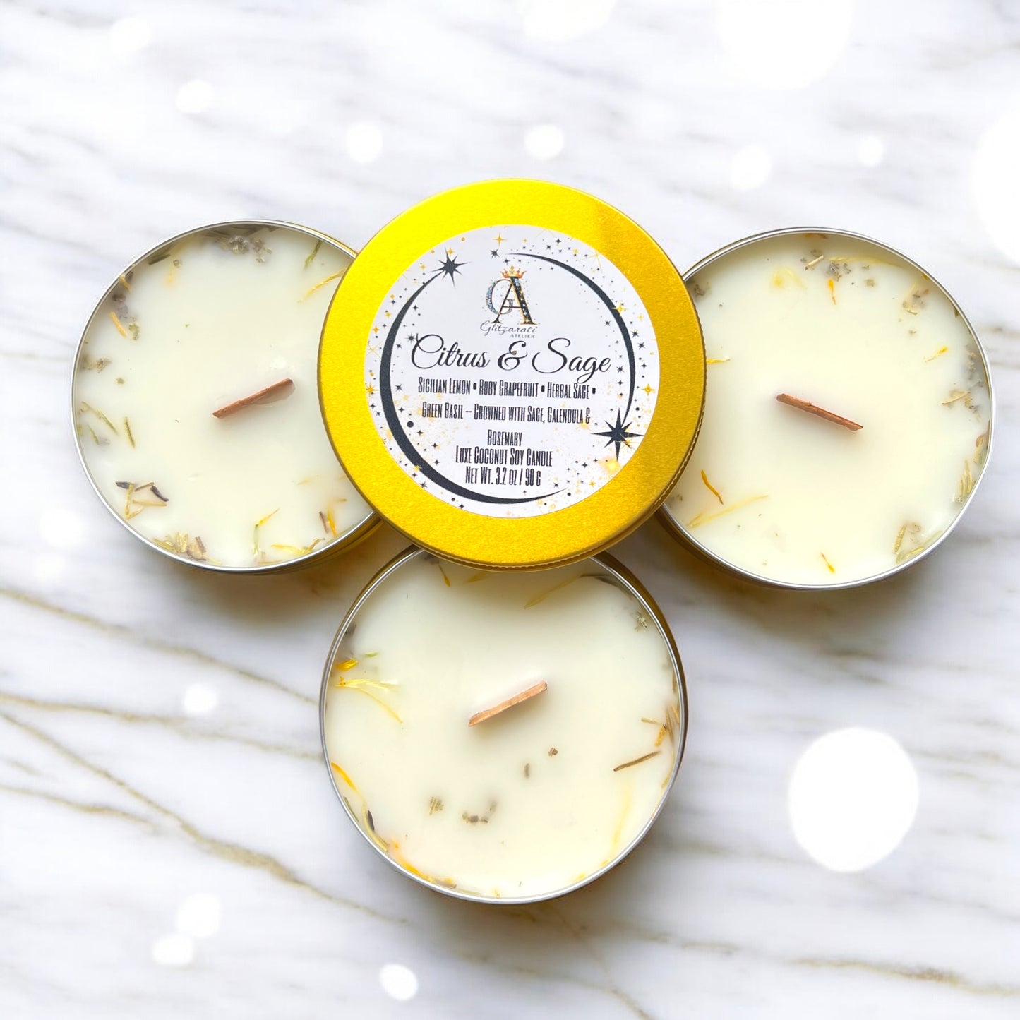 Three small candles in metal tins with a yellow lid on a marble surface
