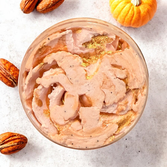 Pumpkin spice latte in a glass with whipped cream, surrounded by pumpkins and pecans on a light background
