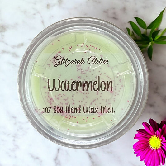 Jar of Glitzerati Atelier Watermelon soy blend wax melt on a marble surface with a pink flower.