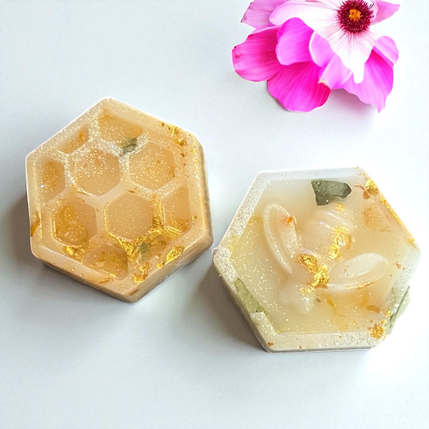 Two hexagonal soap bars with natural patterns on a white background with a pink flower.
