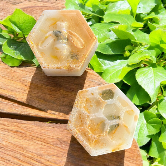 Hexagonal soap bars with natural ingredients on a wooden surface with green leaves in the background