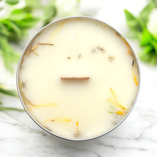 Candle in a metal container with visible wick on a marble surface with greenery in the background