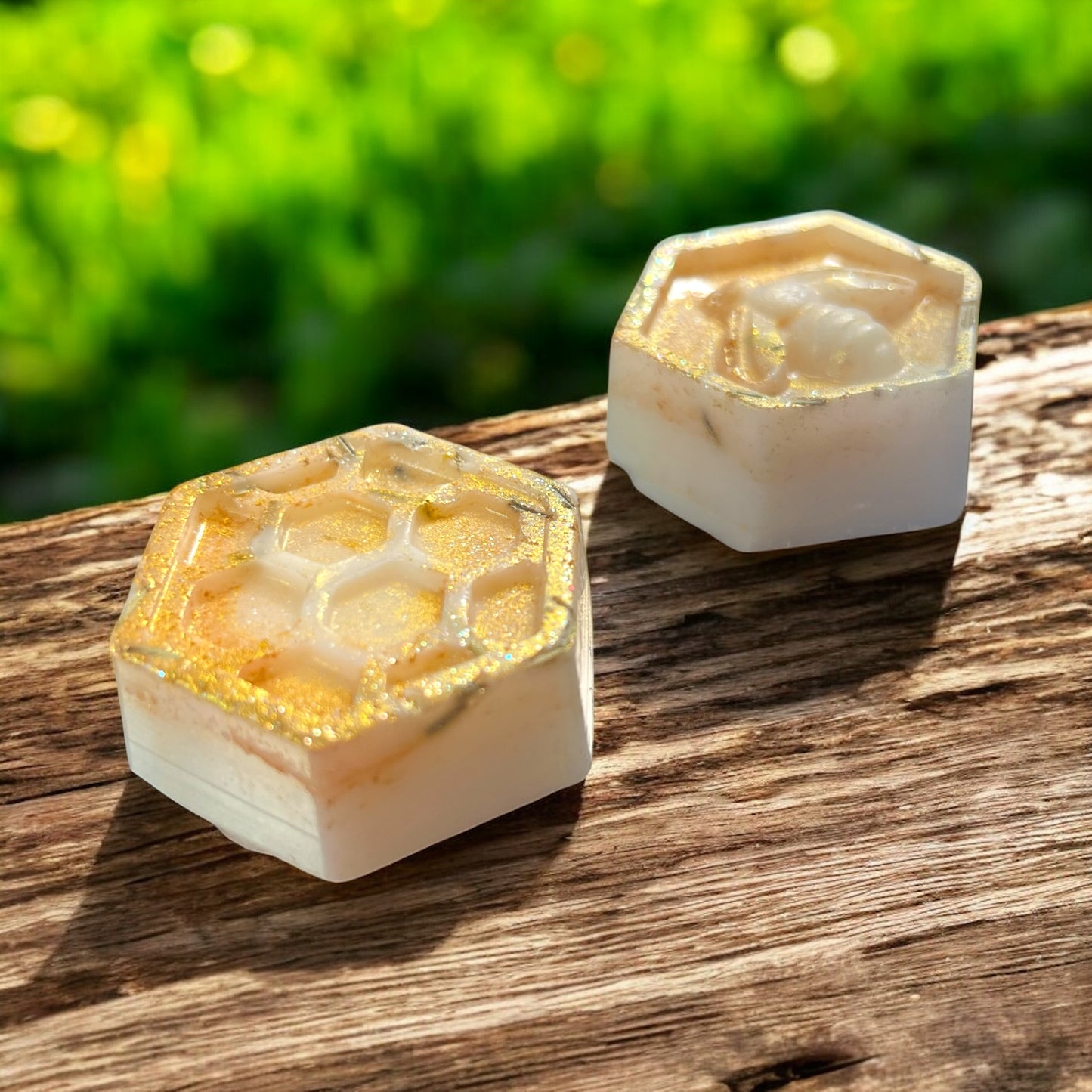 Two hexagonal soap bars with honeycomb design on a wooden surface with a blurred green background