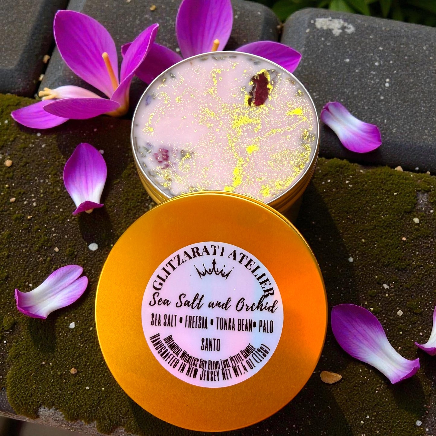 Two containers of sea salt and orchid product with purple flowers on a dark surface