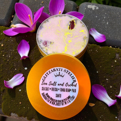 Two containers of sea salt and orchid product with purple flowers on a dark surface