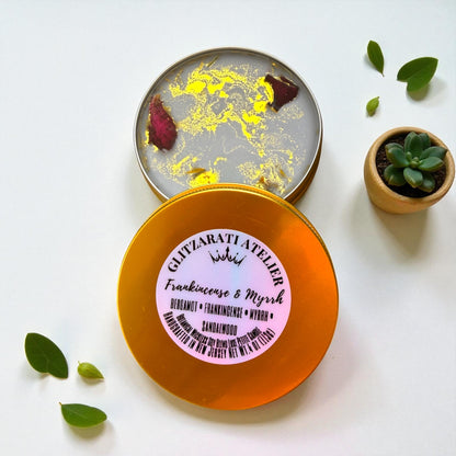 Decorative tin with a label on a white background, surrounded by green leaves and a small plant.