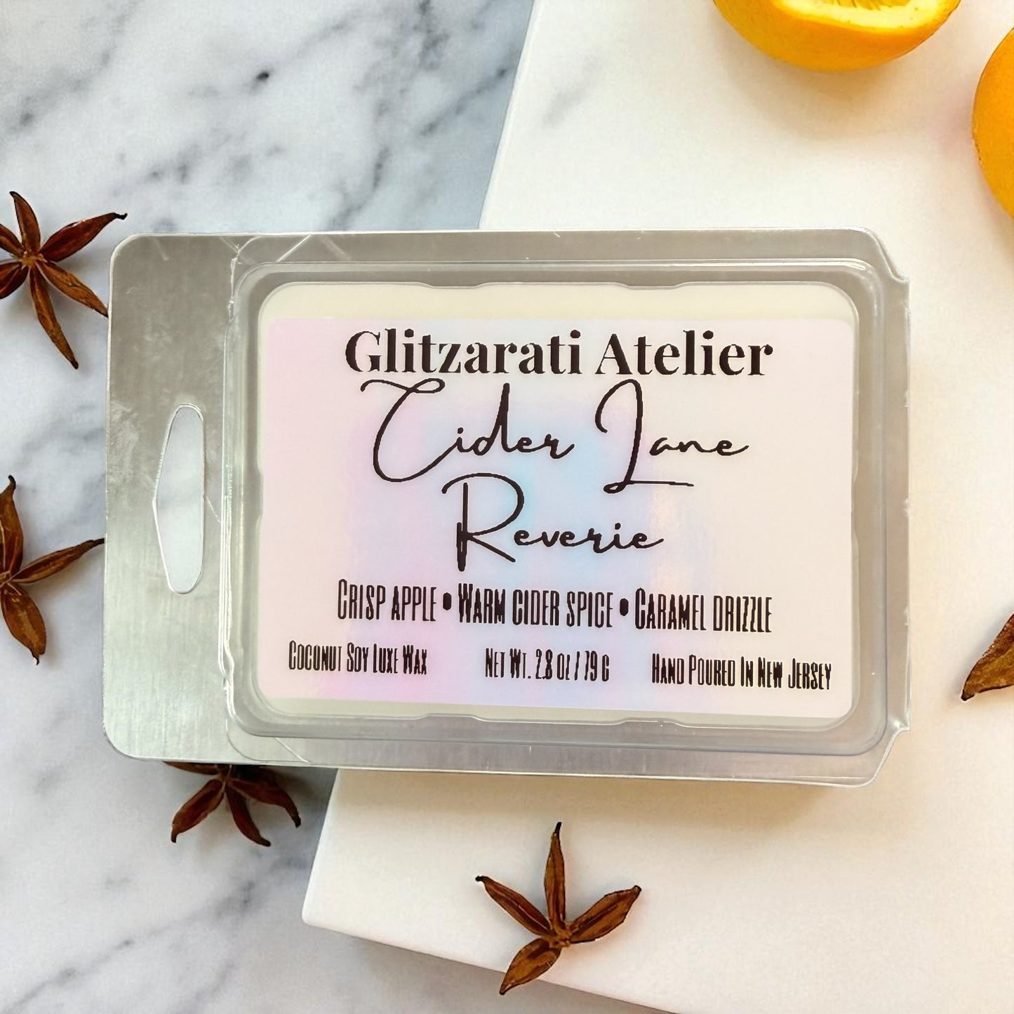 Wax melt packaging with 'Glitzerati Atelier Cider Lane Reverie' label on a marble surface with spices.