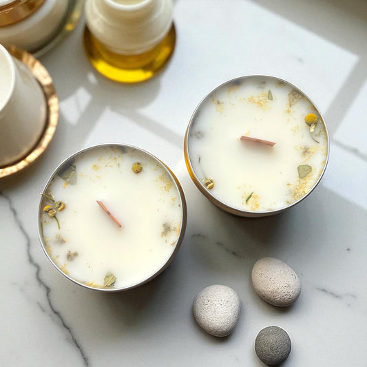 Two small candles with decorative elements on a marble surface with stones.