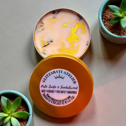 Two tins of scented candles with a plant on a neutral background