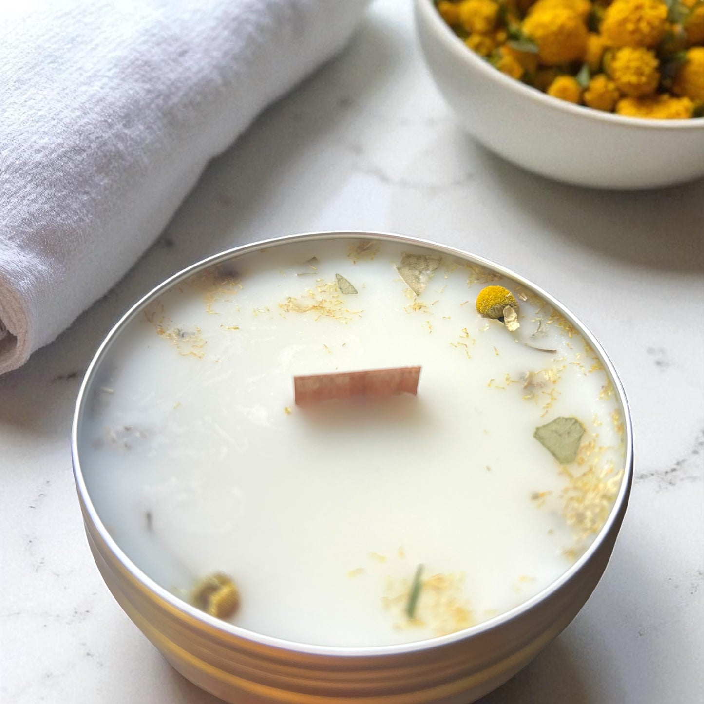 Candle in a glass bowl with floral elements on a marble surface