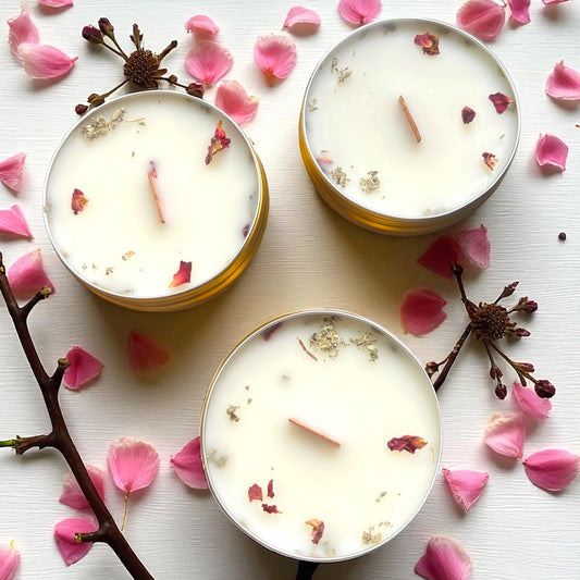 Three white candles with floral elements on a white surface with pink petals and branches.