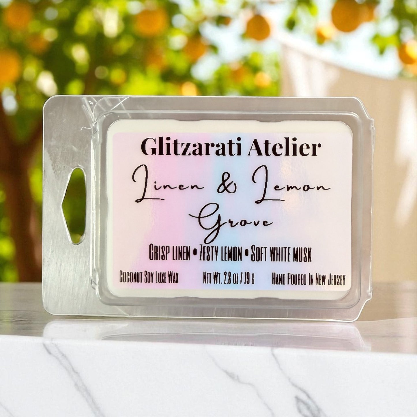 Wax melt container with 'Glitzarati Atelier' branding and product description on a blurred outdoor background.