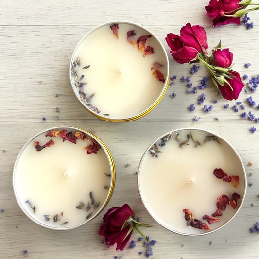 Three small candles with dried flowers on a wooden surface with scattered flowers.