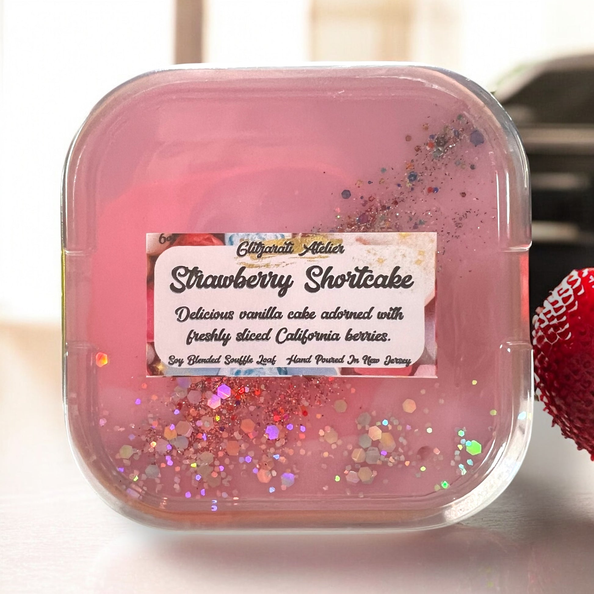 A collection of Glitzarati Atelier's scented wickless wax melt souffles in various colors, presented in aluminized tins surrounded by colorful flowers.
