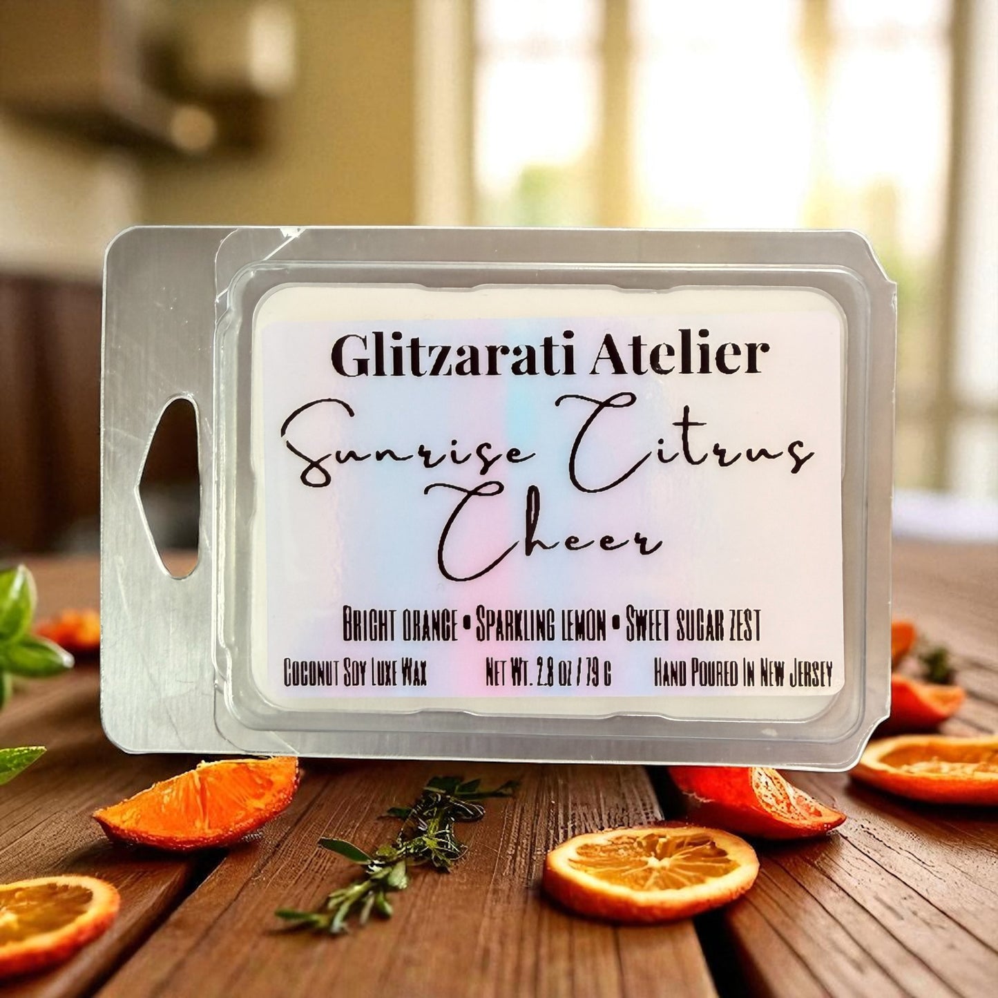 Wax melt packaging with 'Glitzerati Atelier Sunrise Citrus Cheer' on a wooden surface with orange slices.