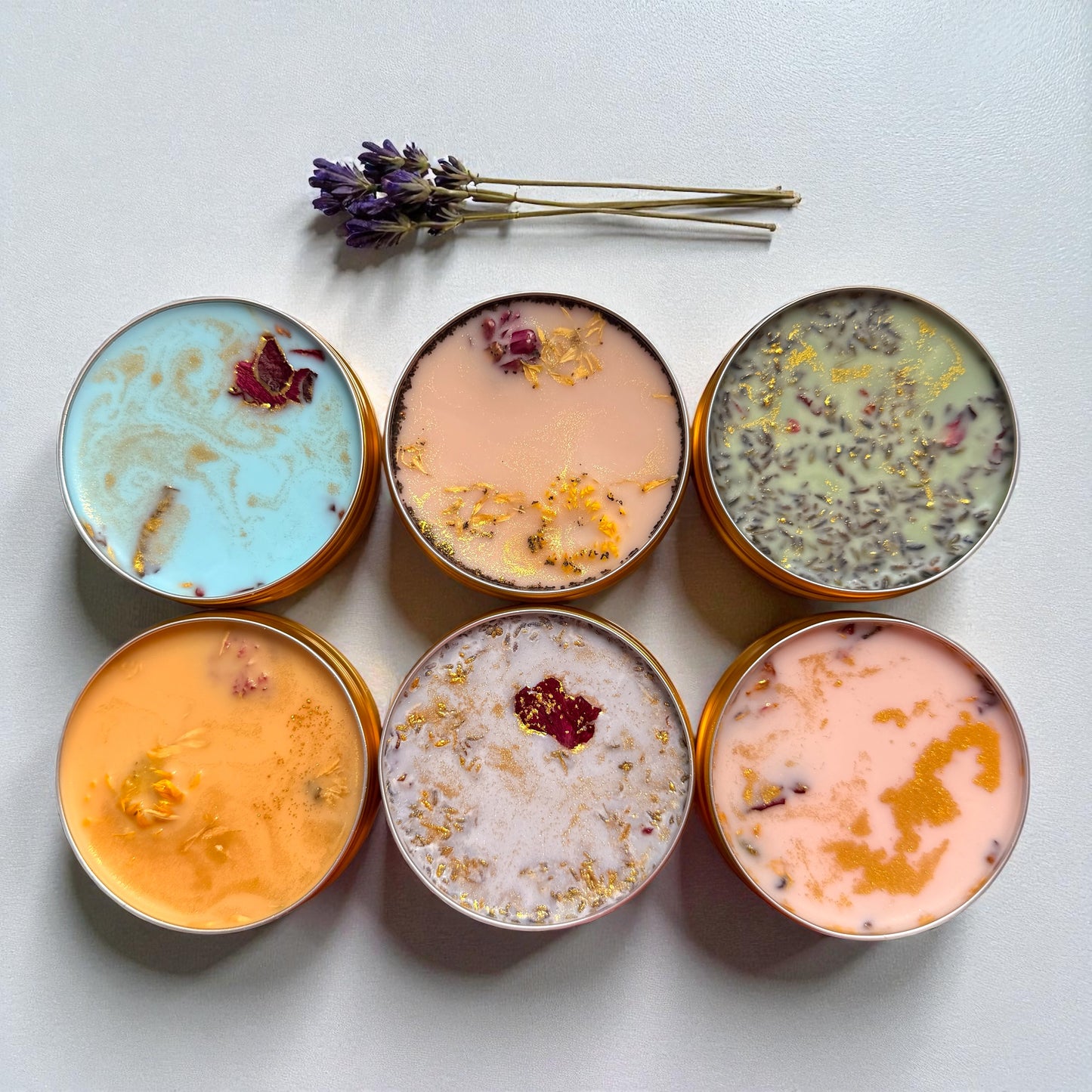 Six small containers with colorful contents on a light surface, accompanied by lavender flowers.