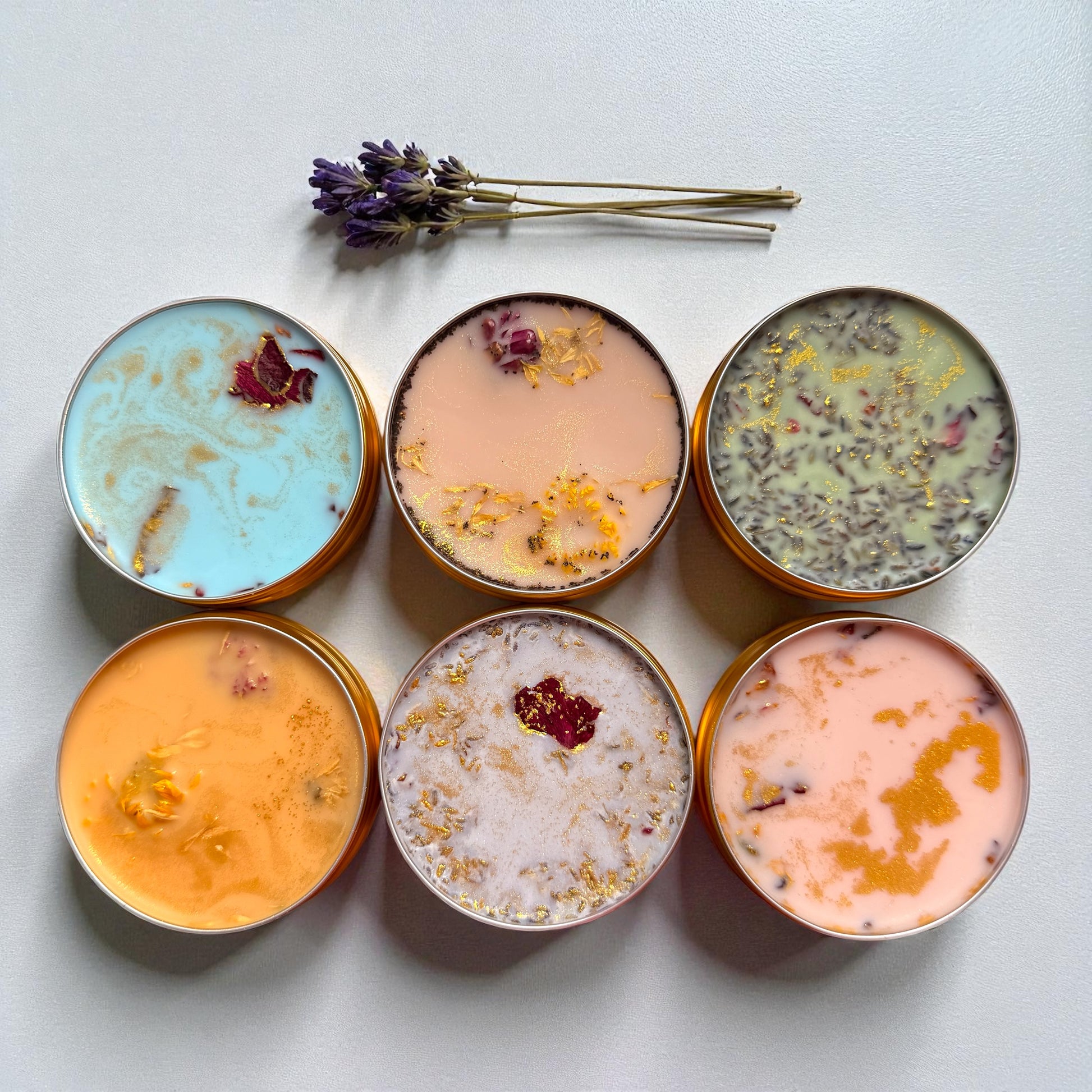 Six small containers with colorful contents on a light surface, accompanied by lavender flowers.