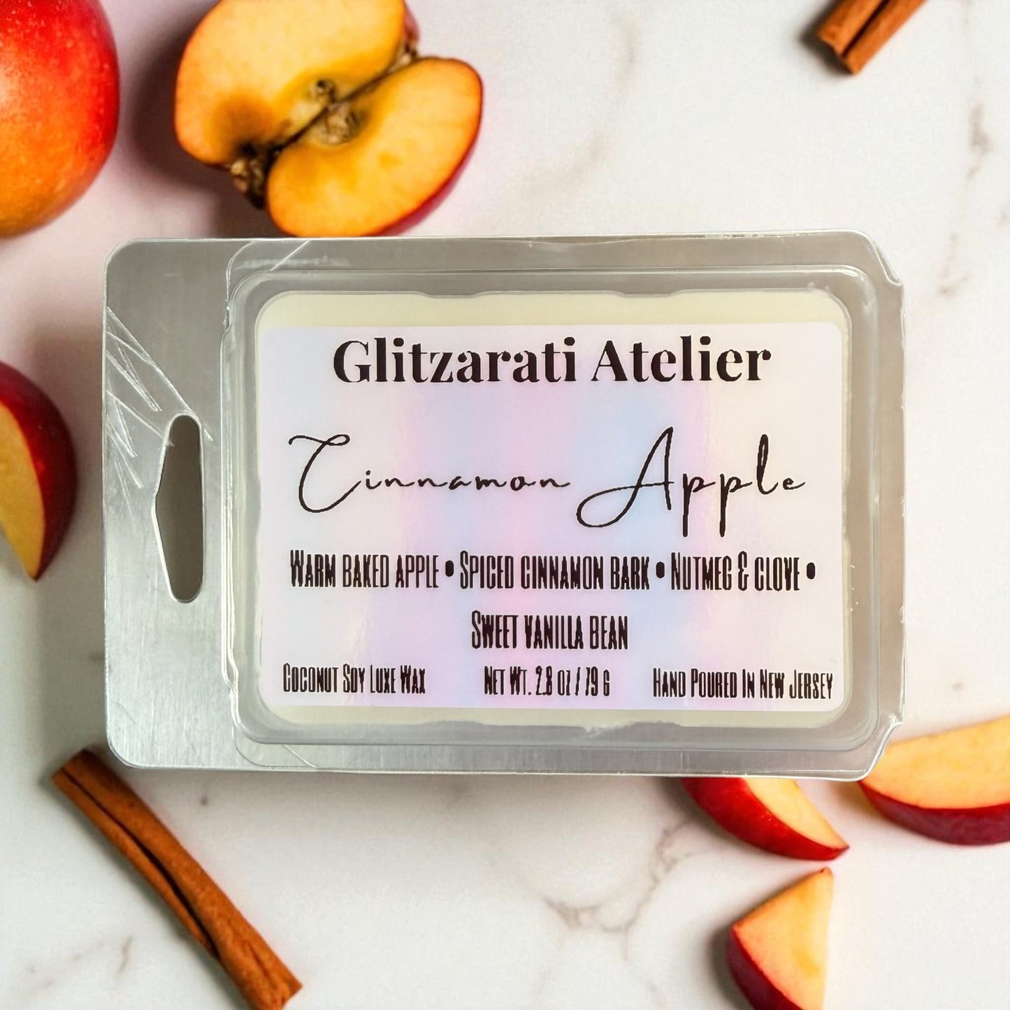 Wax melt packaging with 'Glitzerati Atelier' branding on a background of apples and cinnamon sticks.