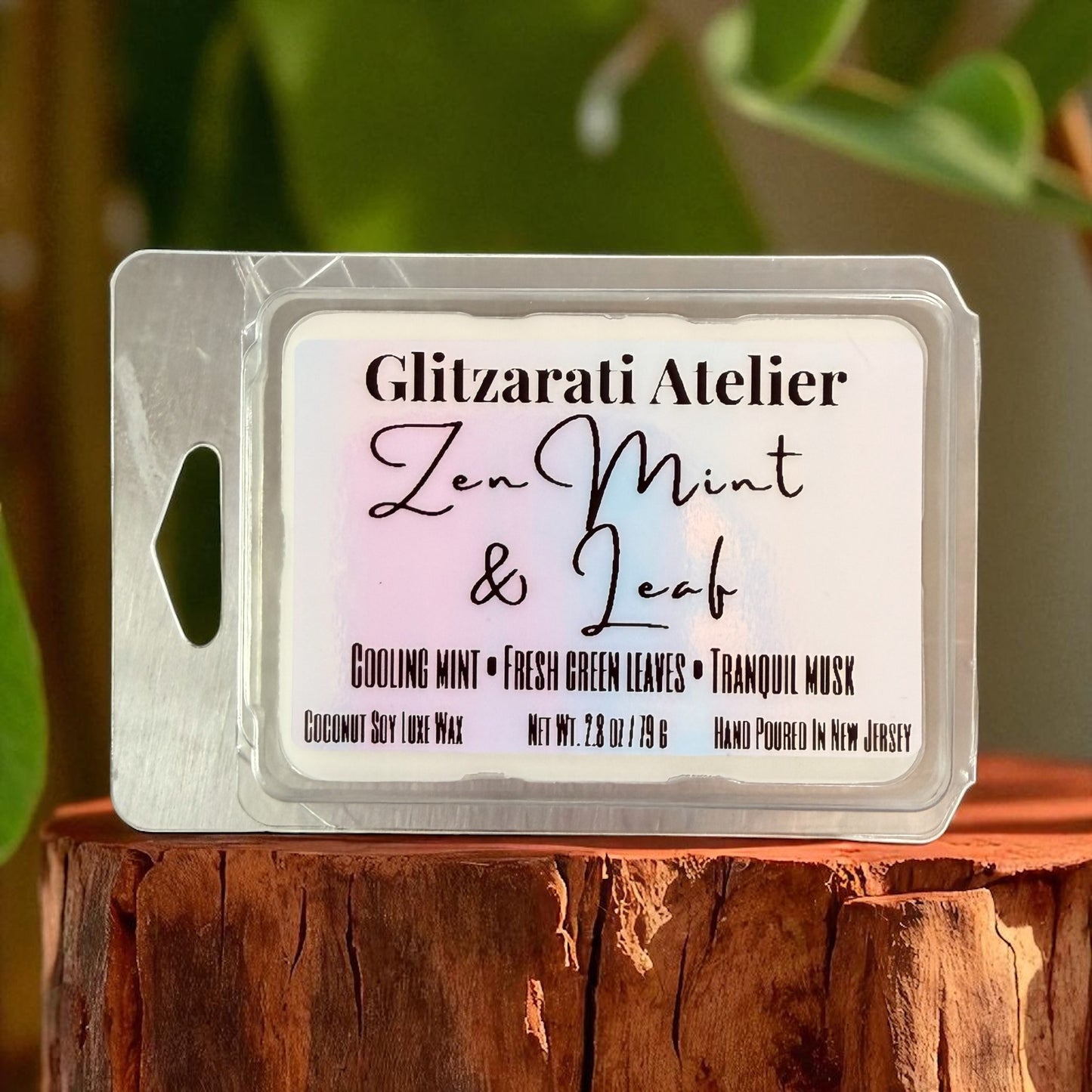 Wax melt packaging with 'Glitzarati Atelier' branding on a wooden surface with greenery in the background.