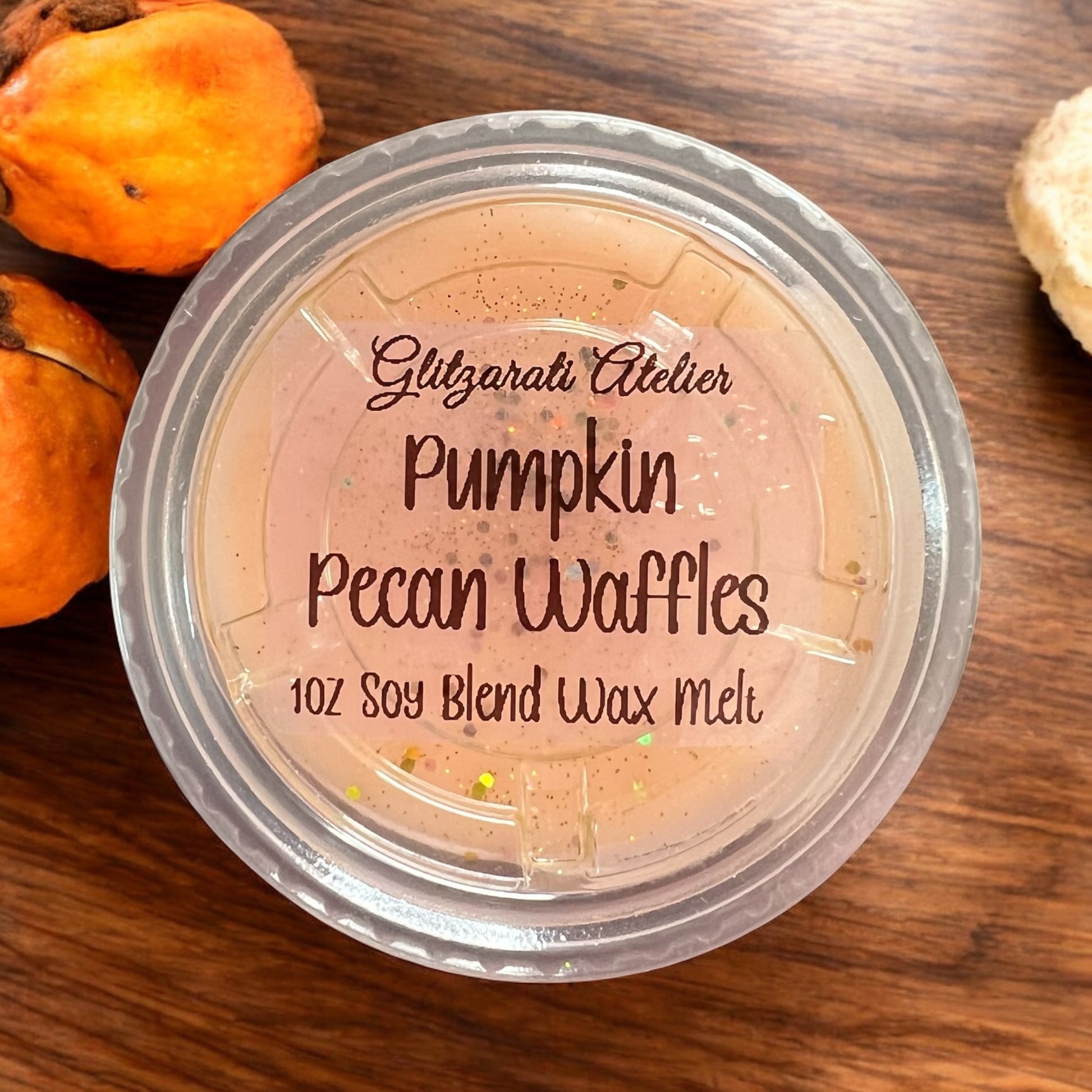 Container of 'Pumpkin Pecan Waffles' wax melt with pumpkins on a wooden surface