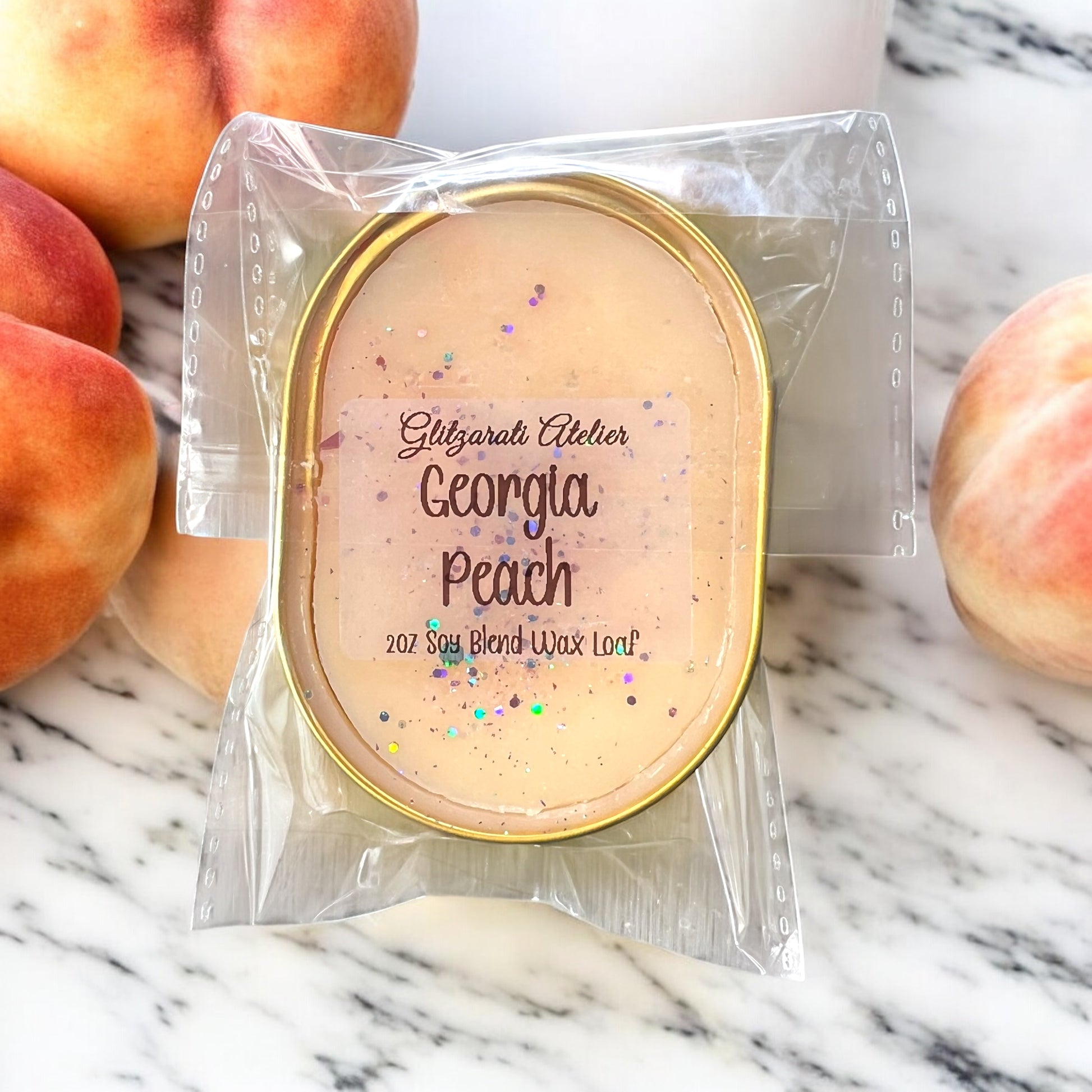 Wax melt packaging labeled 'Georgia Peach' by Glitzarati Atelier on a marble surface with peaches.