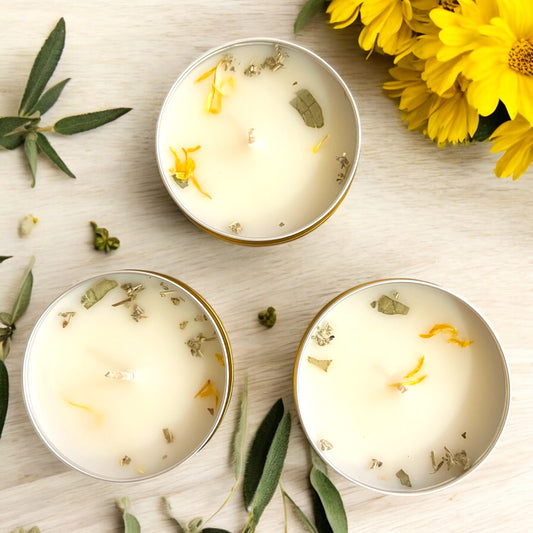 Three small candles with floral elements on a wooden surface with yellow flowers and green leaves.