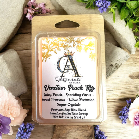 Packaged wax melt with Glitzerati Atelier branding on a wooden surface with flowers.