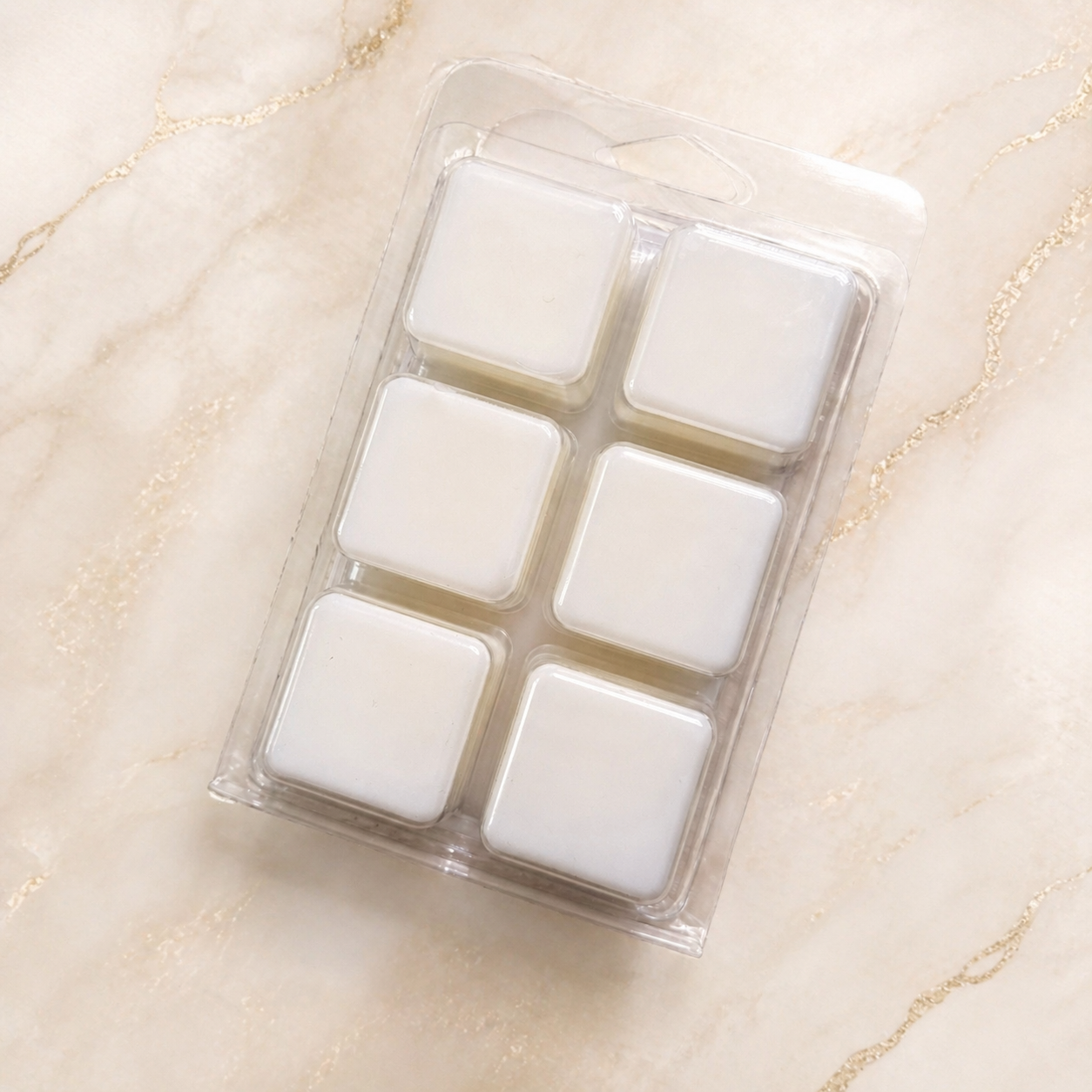 Pack of six white wax melts in clear plastic packaging on a beige marble surface.
