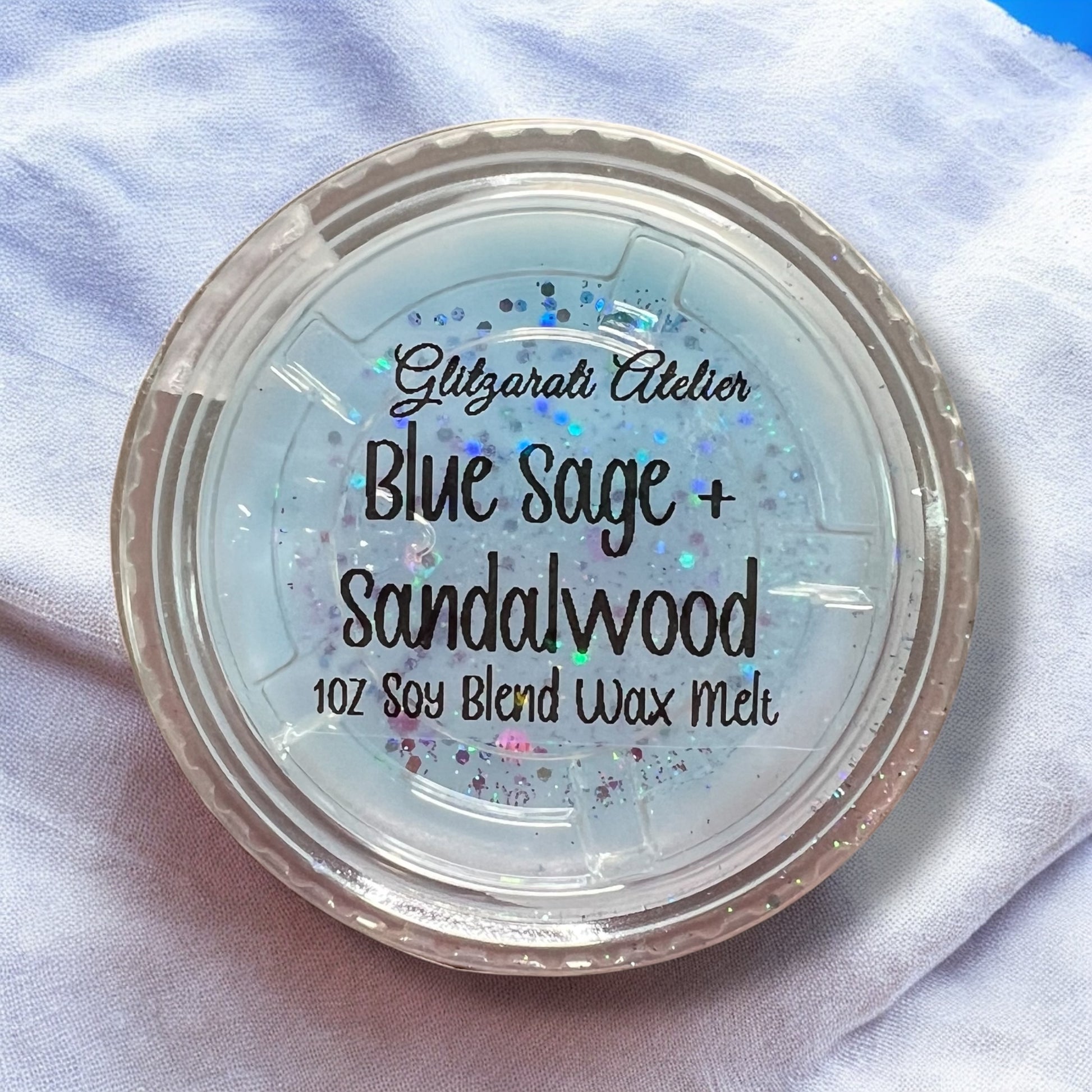 Soy blend wax melt container labeled 'Blue Sage + Sandalwood' on a light fabric background