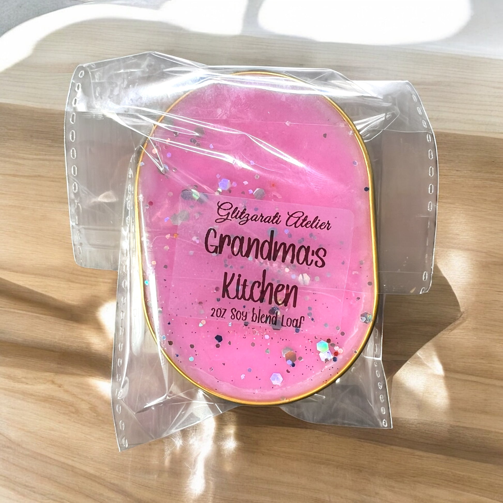 Pink soap bar with 'Grandma's Kitchen' text in clear packaging on a wooden surface