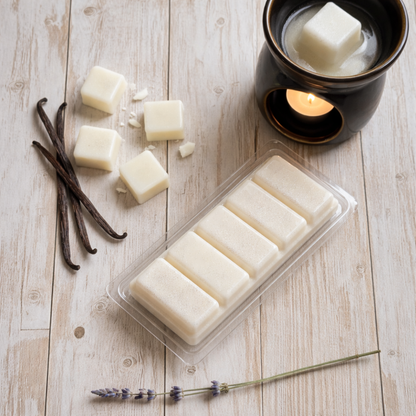 White wax melts in a clear container on a wooden surface with vanilla beans and lavender.