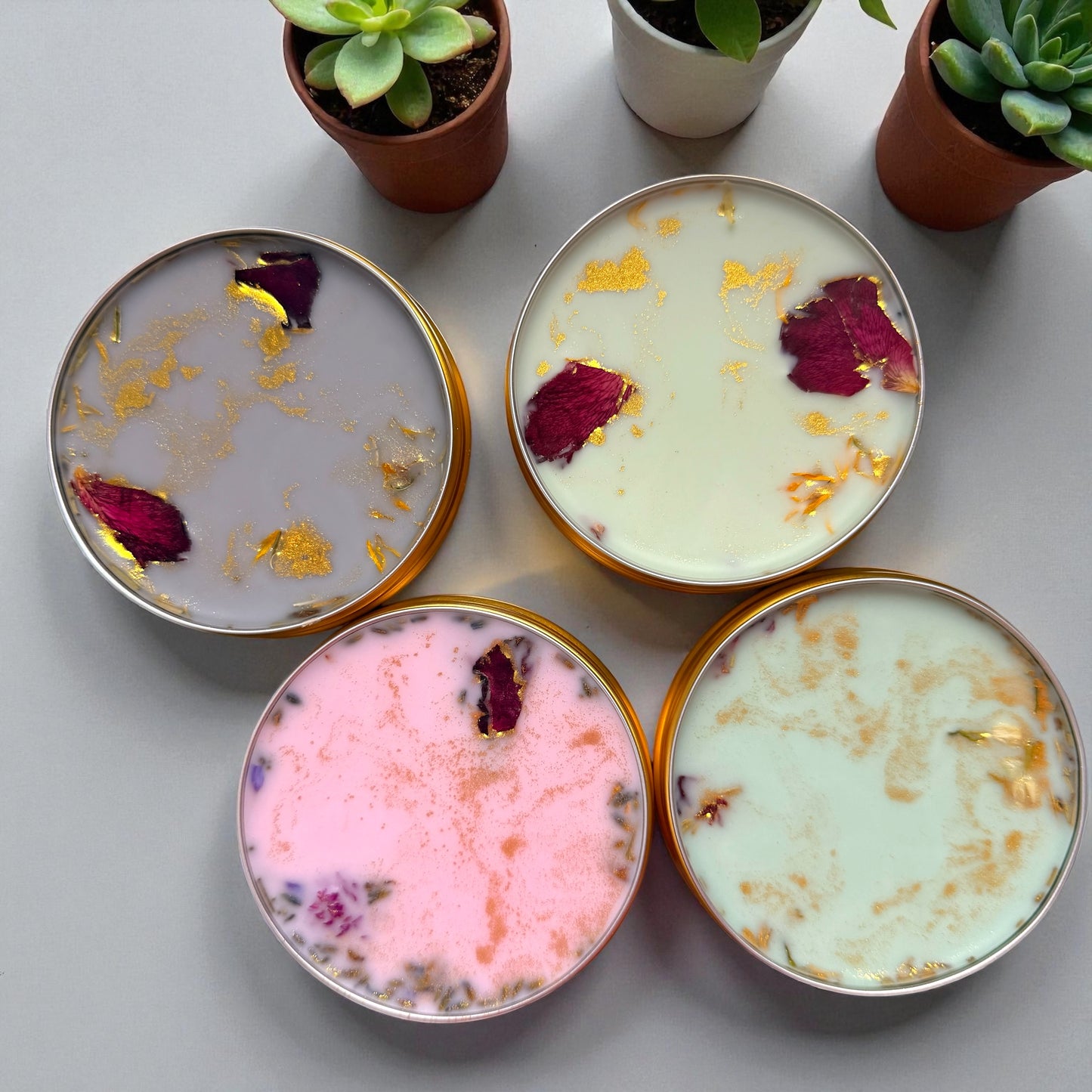 Four small containers with decorative contents on a light surface with potted plants in the background.