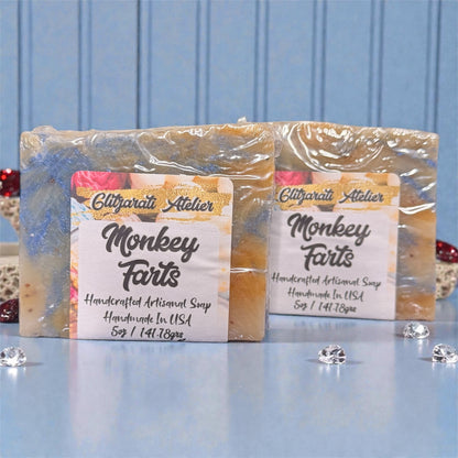 Two bars of soap labeled 'Monkey Farts' with Elitparati Atelier branding on a blue background.