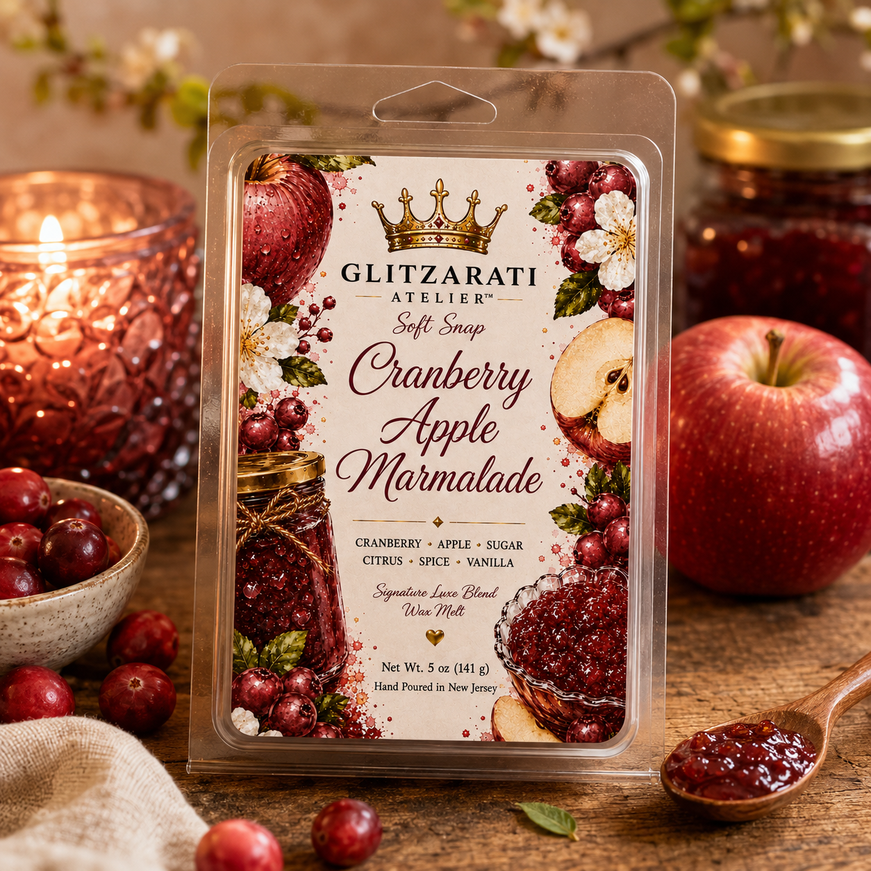 Glitzarati Atelier Cranberry Apple Marmalade wax melt packaging with apples, cranberries, and a candle in the background.