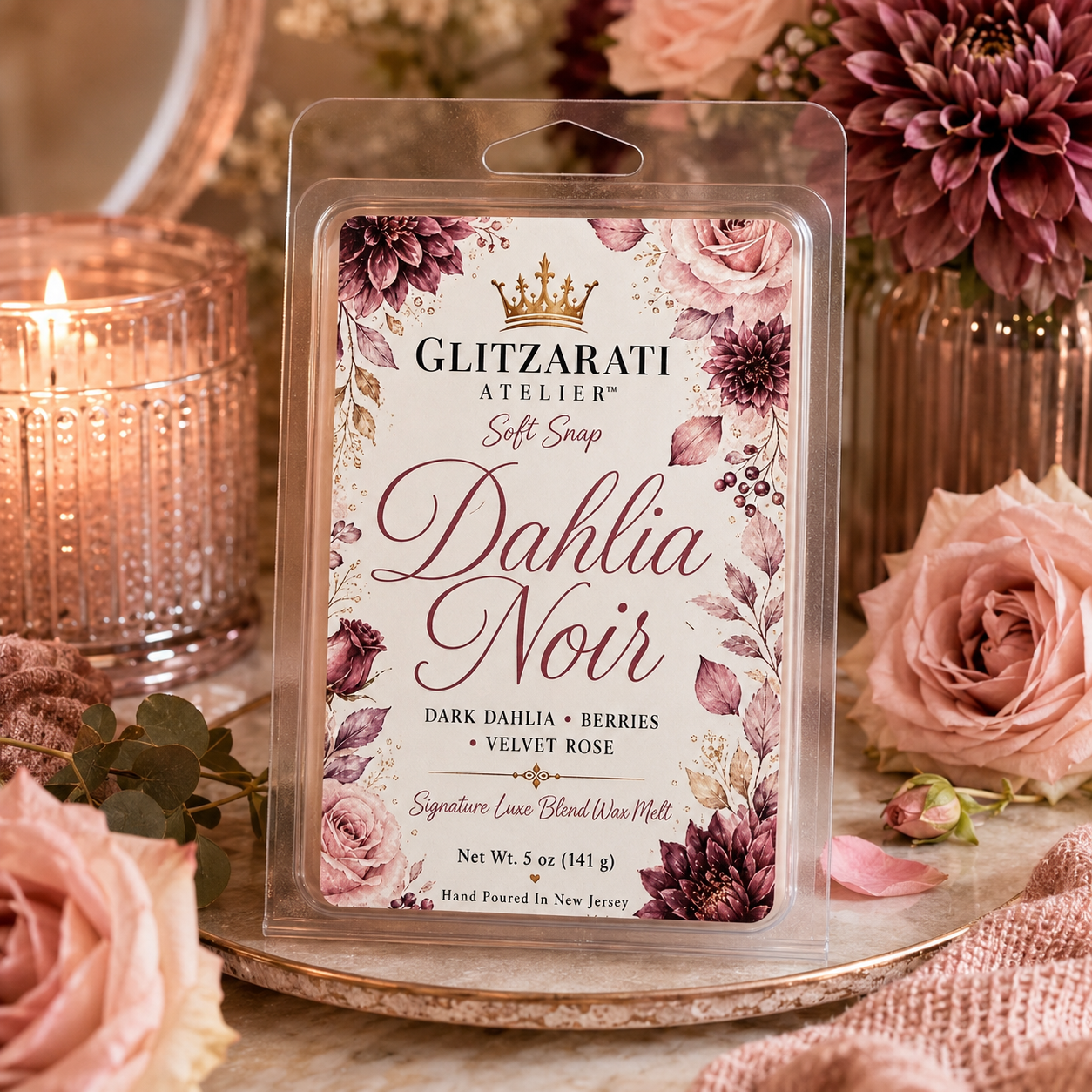 Glitzarati Atelier Dahlia Noir wax melt packaging with floral design, surrounded by roses and a candle.