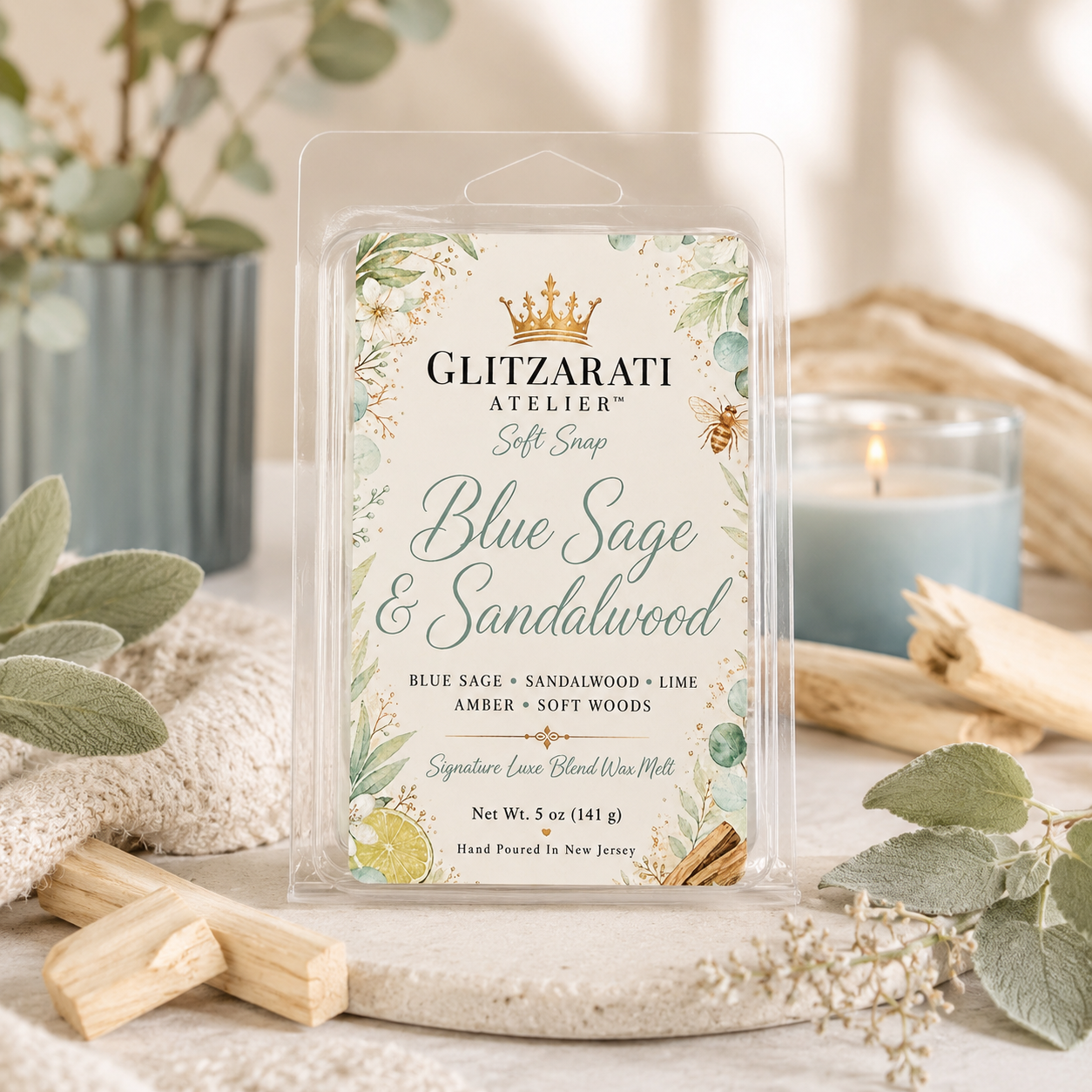 Glitzarati Atelier Blue Sage & Sandalwood wax melt packaging on a decorative surface with plants and candles.