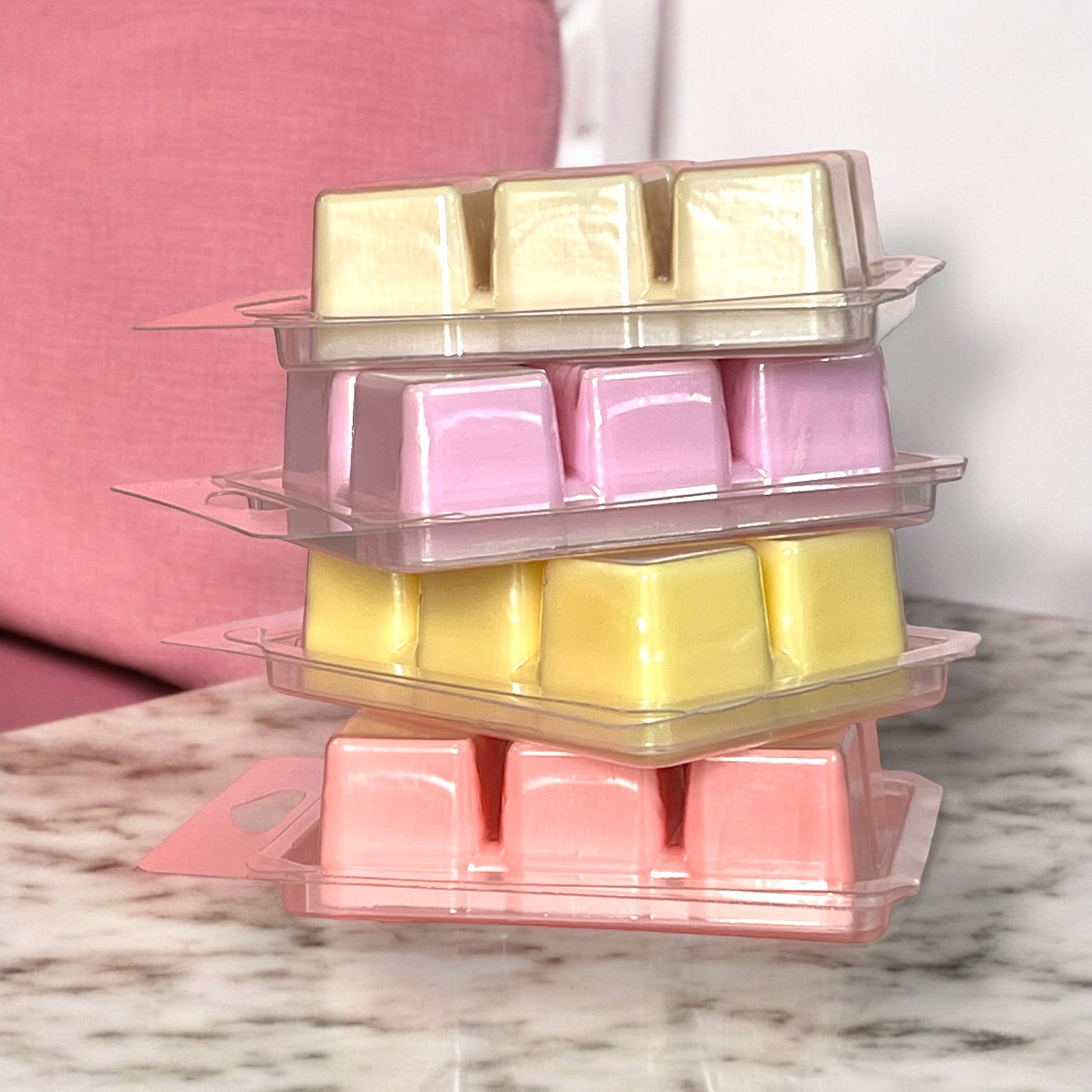 Stack of clear plastic containers with yellow, pink, and red wax cubes on a marble surface.