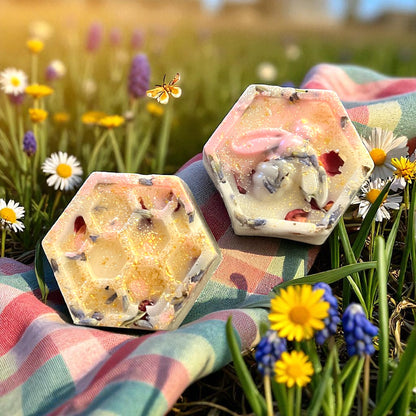 Hexagonal soap bars with natural ingredients on a colorful towel surrounded by flowers and grass.
