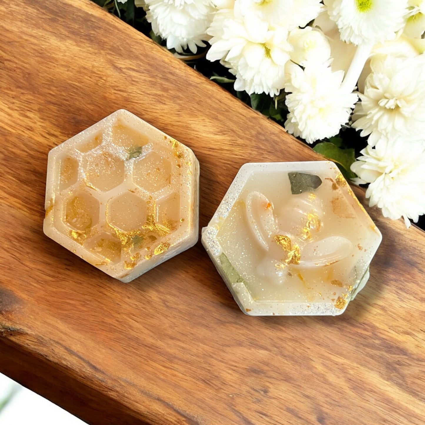 Two hexagonal honeycomb-shaped soaps on a wooden surface with white flowers in the background.