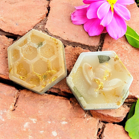 Two hexagonal honeycomb-shaped candles on a brick surface with a pink flower.