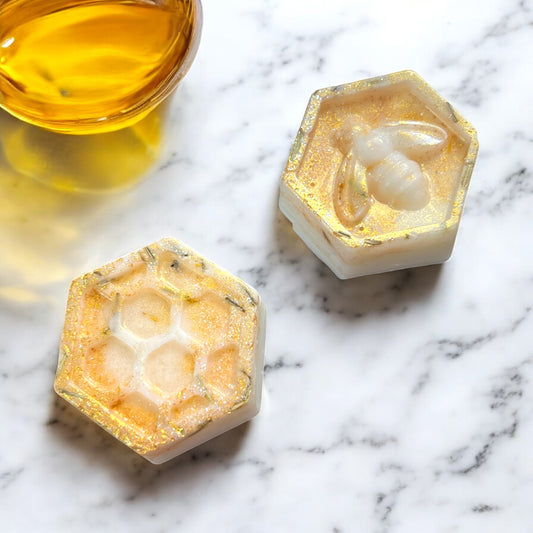 Two hexagonal soap bars with honeycomb design on a marble surface.