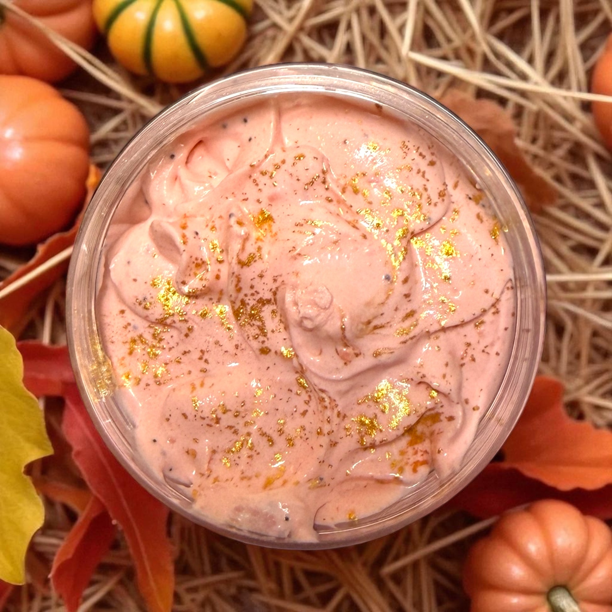 Pink slime with gold glitter in a clear container surrounded by pumpkins and leaves