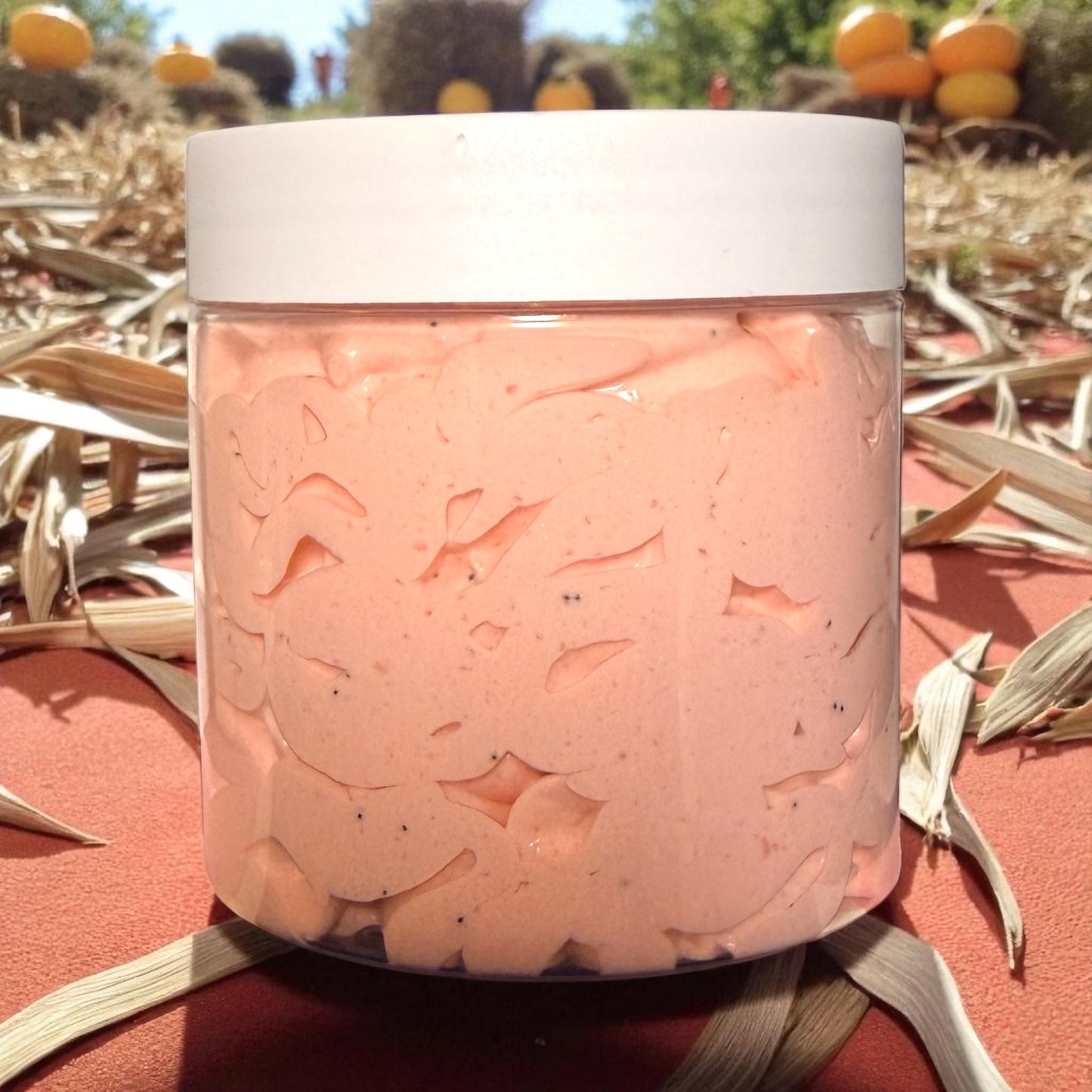 Jar of pink bath salts with a white lid, set against a natural background with pumpkins and corn stalks.
