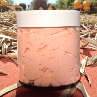 Jar of pink bath salts with a white lid, set against a natural background with pumpkins and corn stalks.