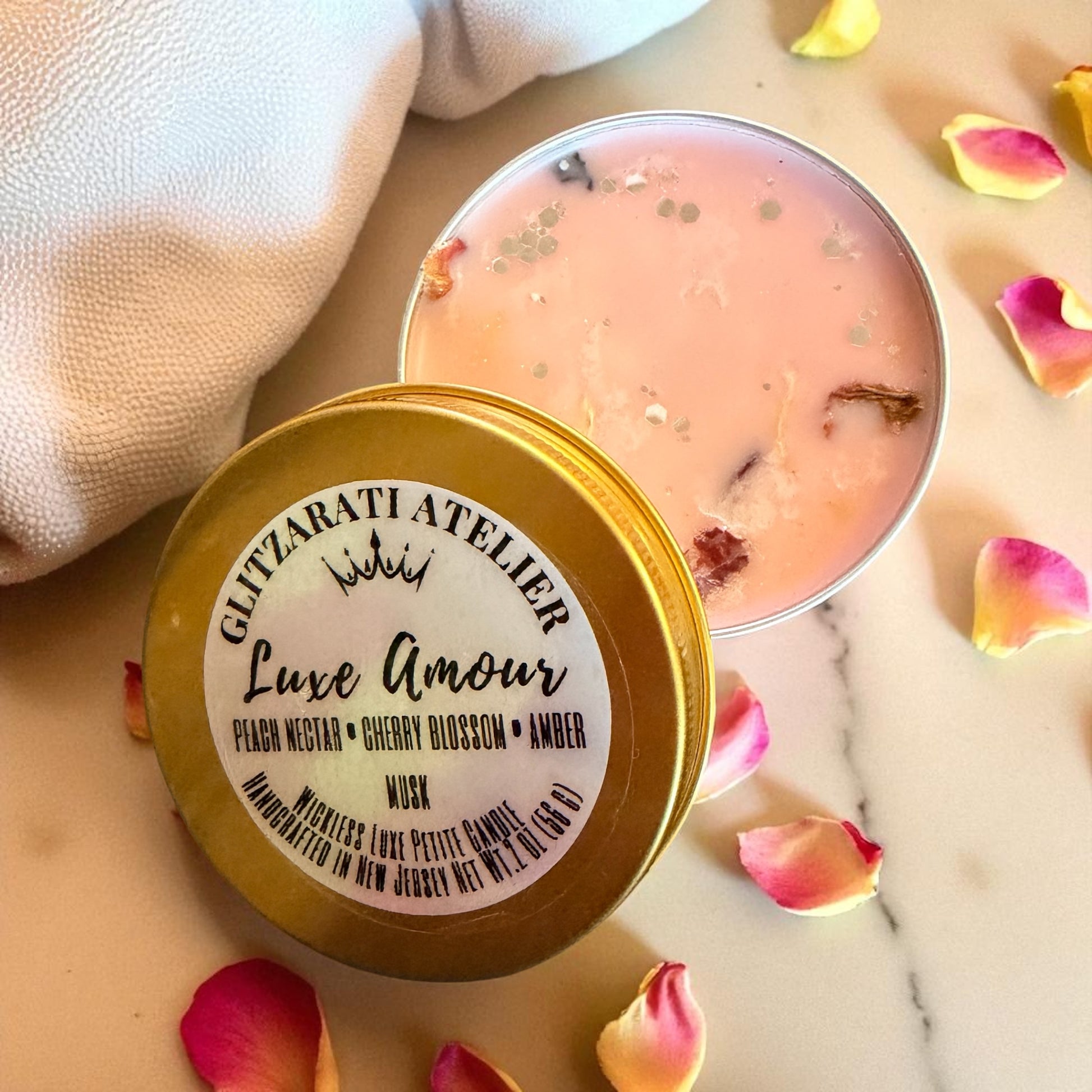 Luxury candle with 'Glitzarati Atelier' branding on a marble surface with rose petals.