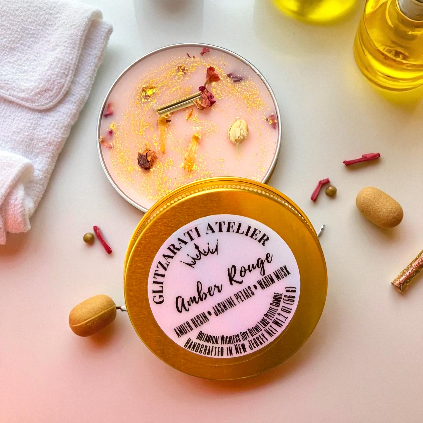 Candle with decorative elements on a light surface, featuring 'Glitzarati Atelier' branding.